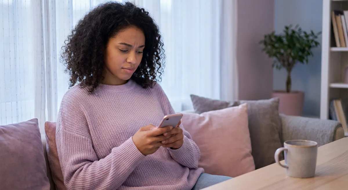 Mujer joven mirando su celular con expresión de angustia representando la dependencia emocional a distancia.