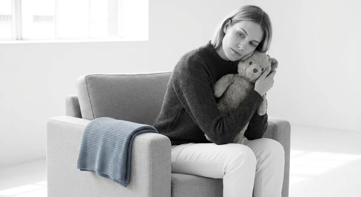 Madre abrazando un oso de peluche con expresión de tristeza simbolizando la pérdida gestacional y el proceso de duelo.
