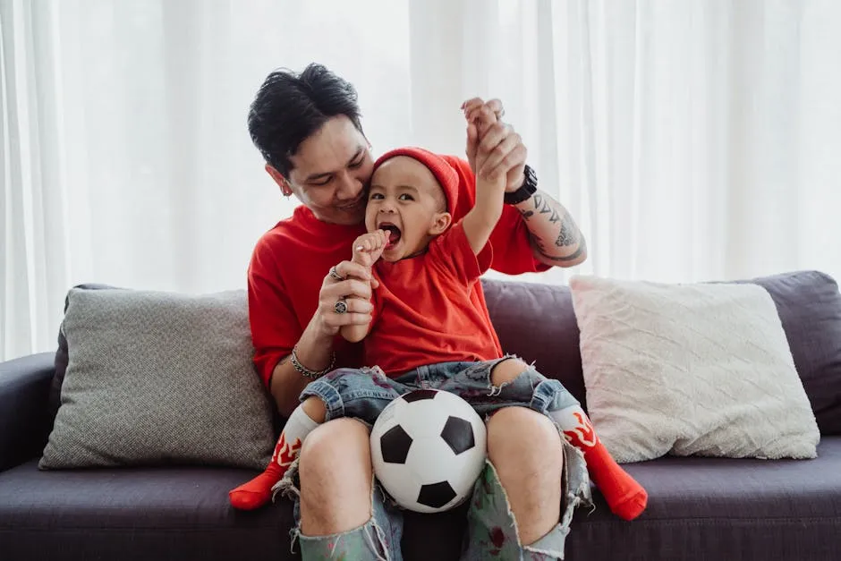 Padre e hijo sentados en el sillón viendo un partido de fútbol y compartiendo una expresión de alegría.
