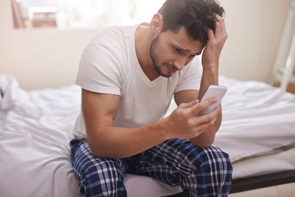 Hombre sentando en su cama viendo su celular
