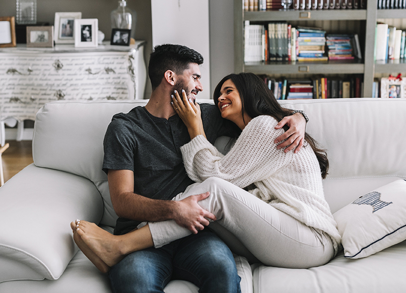 Pareja en su departamento, sentada en un sofa blanco siendo felices uno al otro.