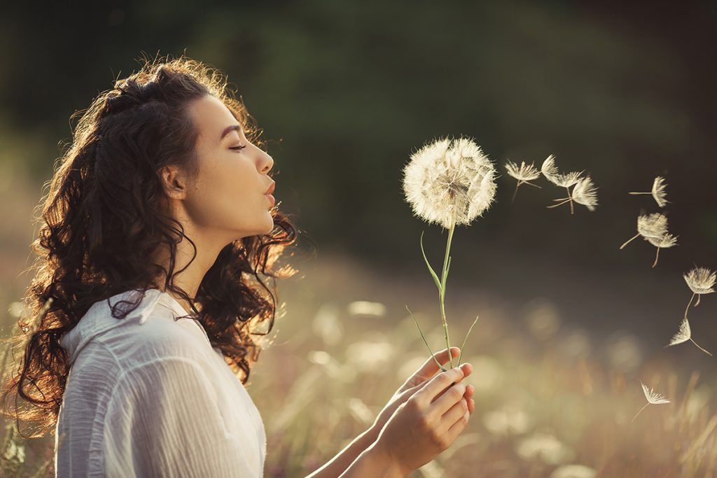 Mujer en el campo soplando un diente de leon felizmente.