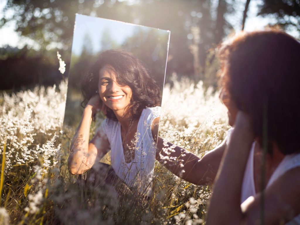 Mujer en la pradera feliz por superar su relación pasada mientras observa un reflejo de ella en la montaña