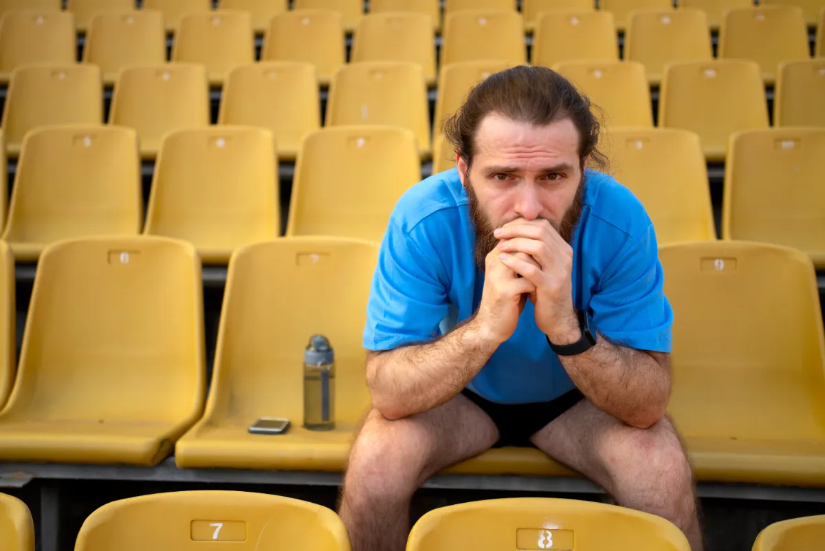Aficionado de fútbol cabizbajo en el estadio tras la derrota de su equipo nacional representando duelo deportivo.